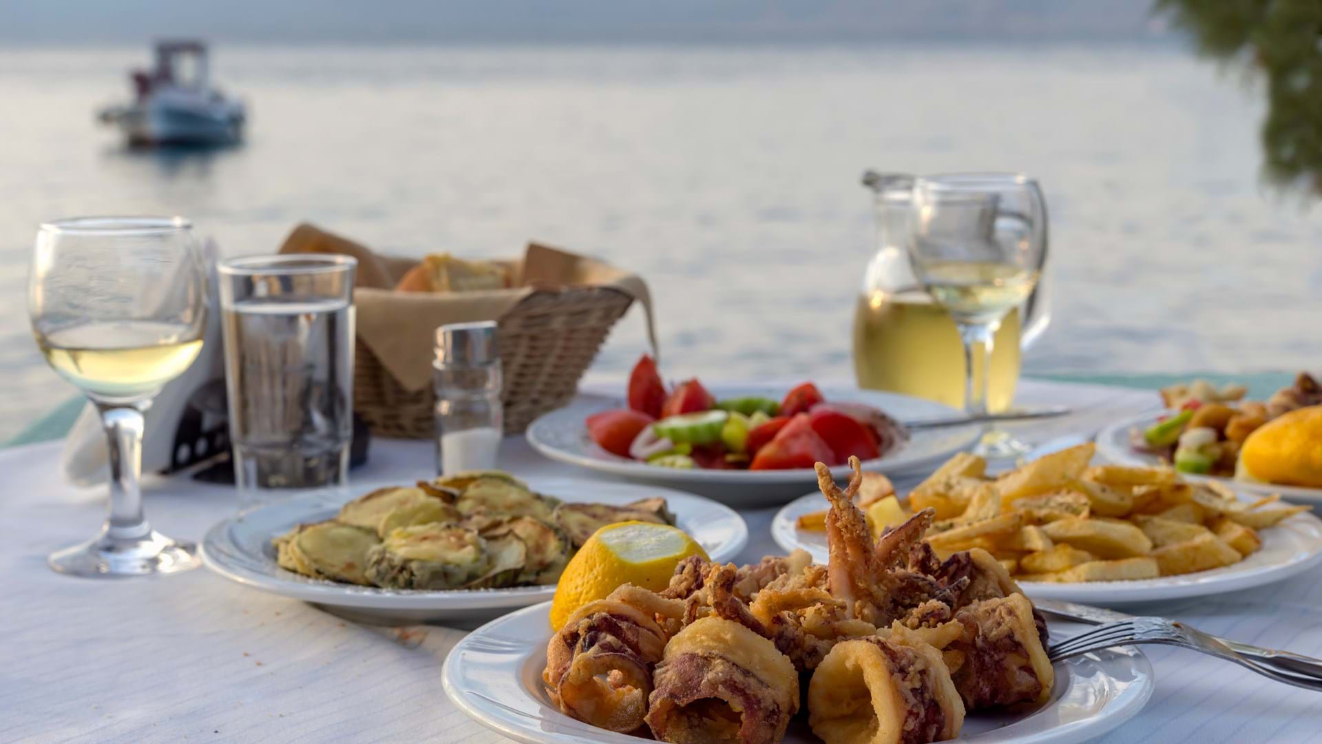 Traditional greek food, with fresh calamari, fries, cucumber, fried zucchini and tomato salad, served at a greek tavern by the sea. Image taken in the sunset.